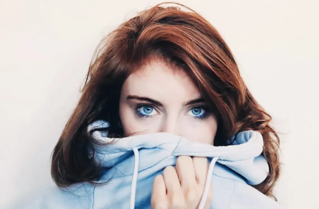 Woman with striking blue eyes, half-hidden in a hoodie.
