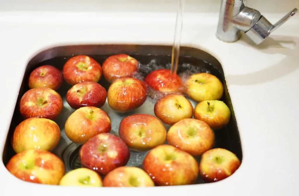 Apples in a sink being cleaned with running water.
