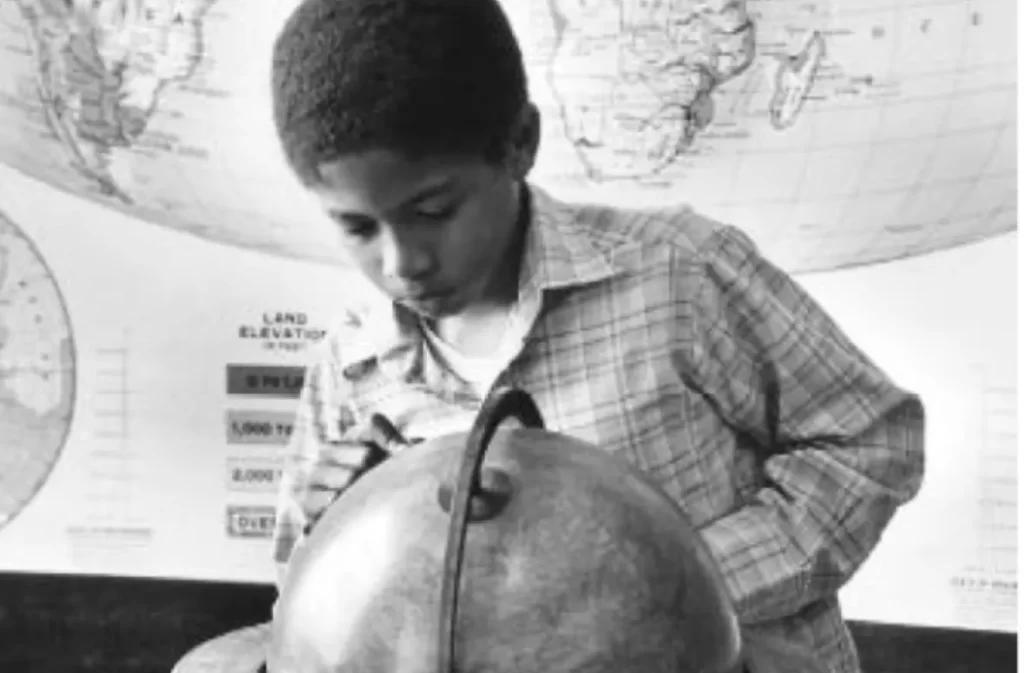 Child studying a globe with a world map in the background.