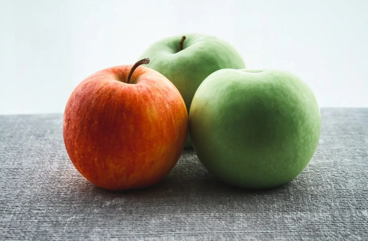 Three apples: one red, two green, on a gray surface.