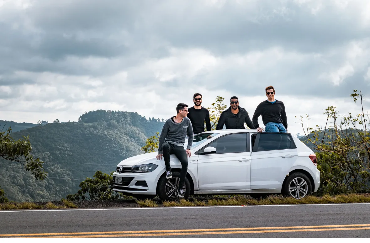 Group enjoying a road trip, leaning on a car by the roadside.