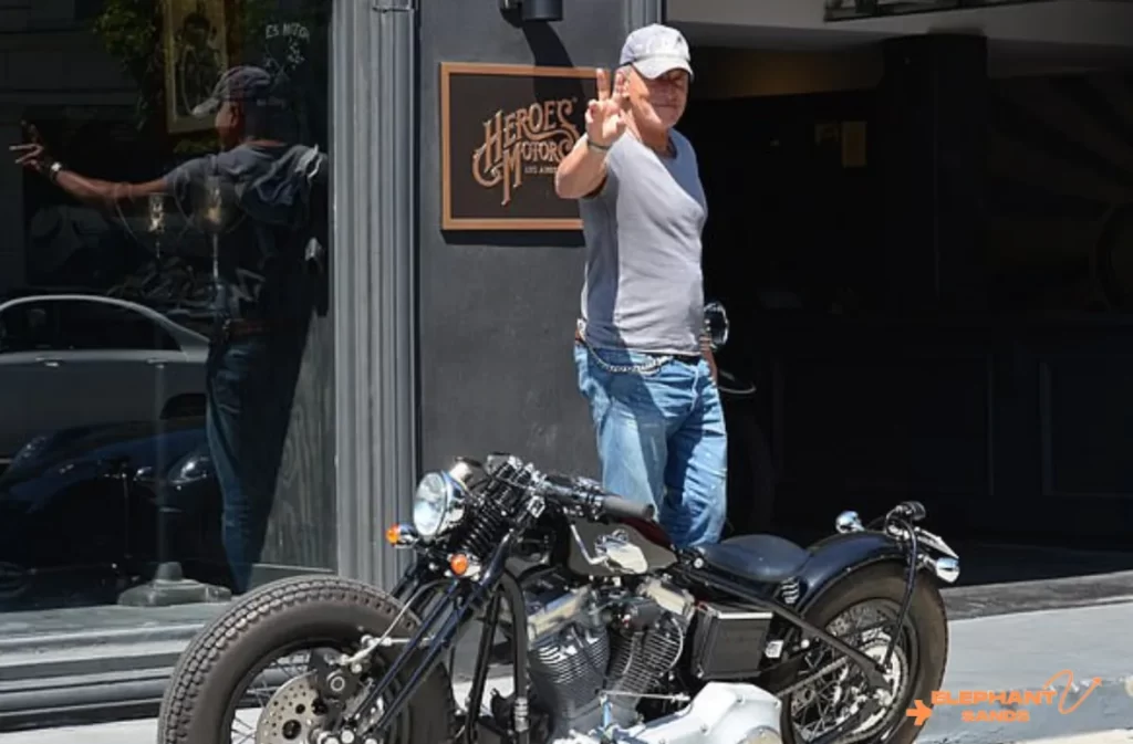 A man in casual wear standing beside a custom Harley-Davidson.