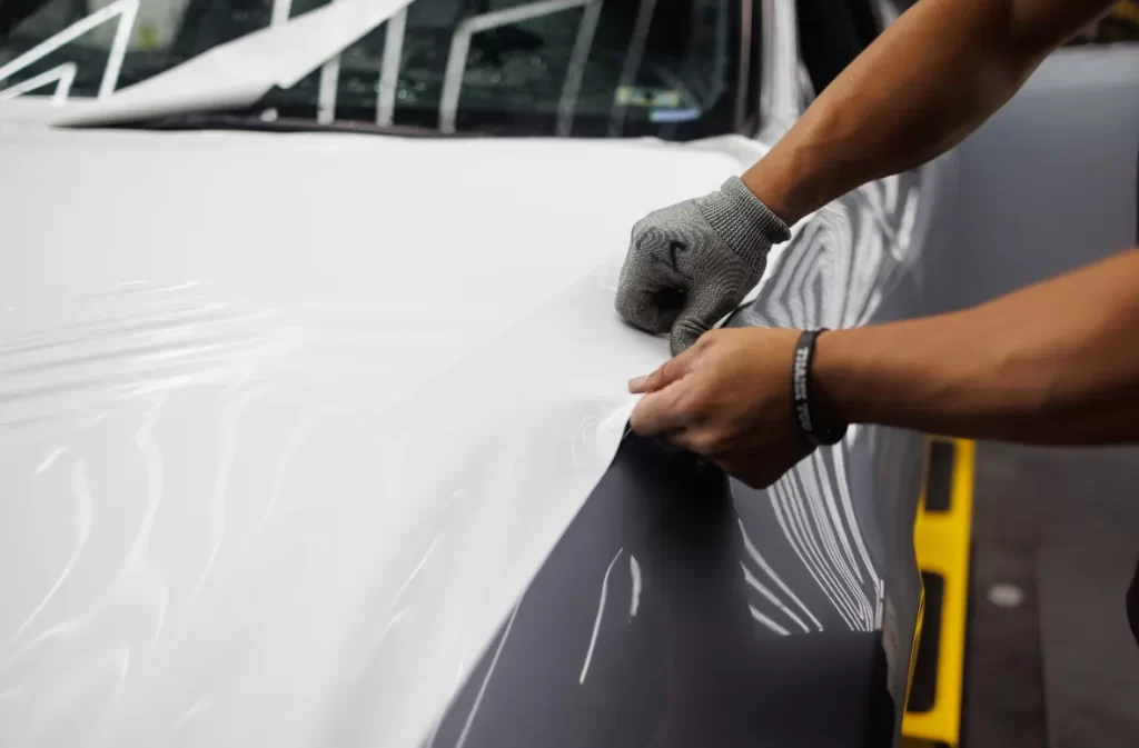 Hands applying a white wrap on a car hood.