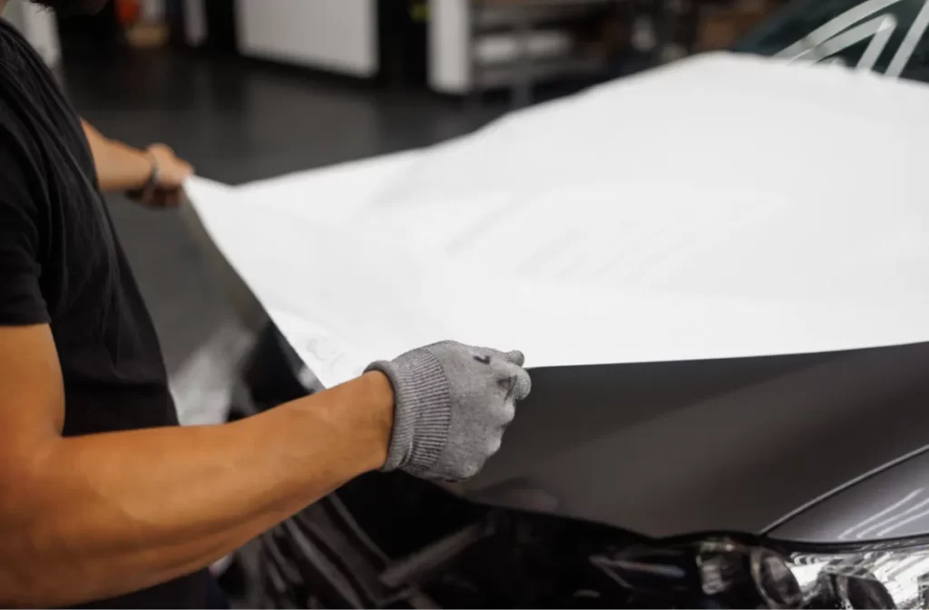 Worker aligning a white wrap over a car's front.