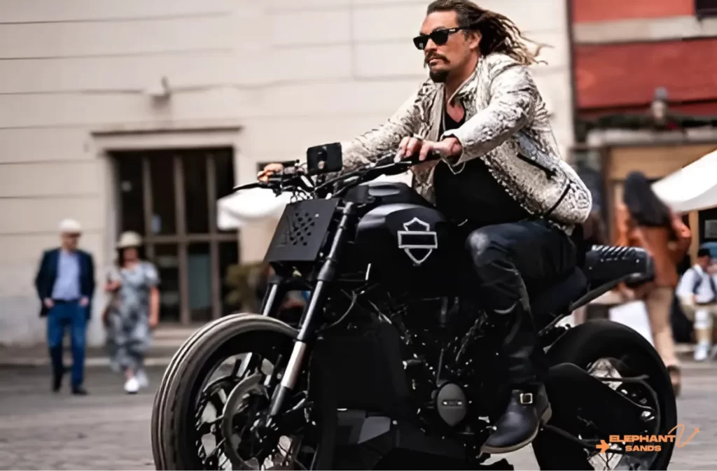 A man with dreadlocks riding a black Harley-Davidson in a city.