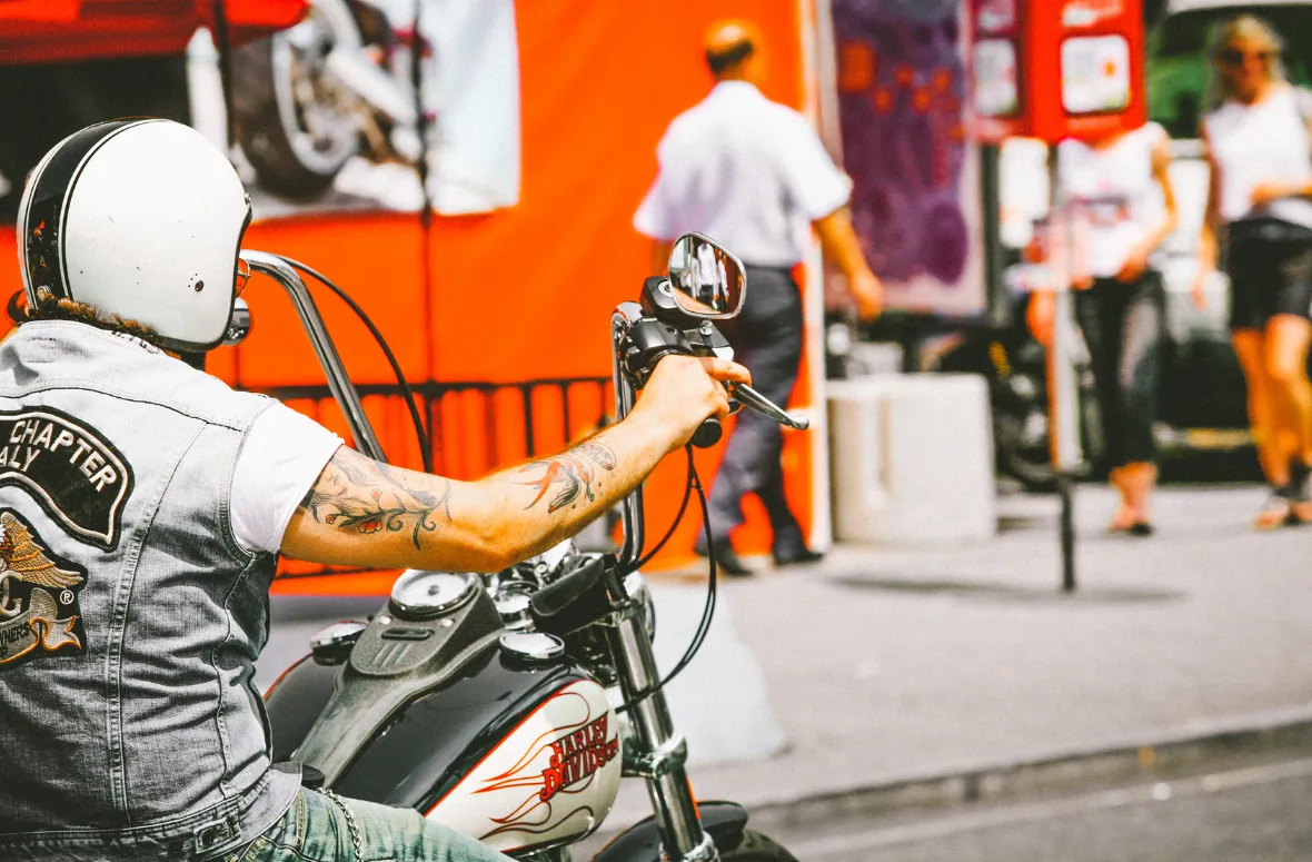 A biker riding a Harley-Davidson with tattoos and a helmet.