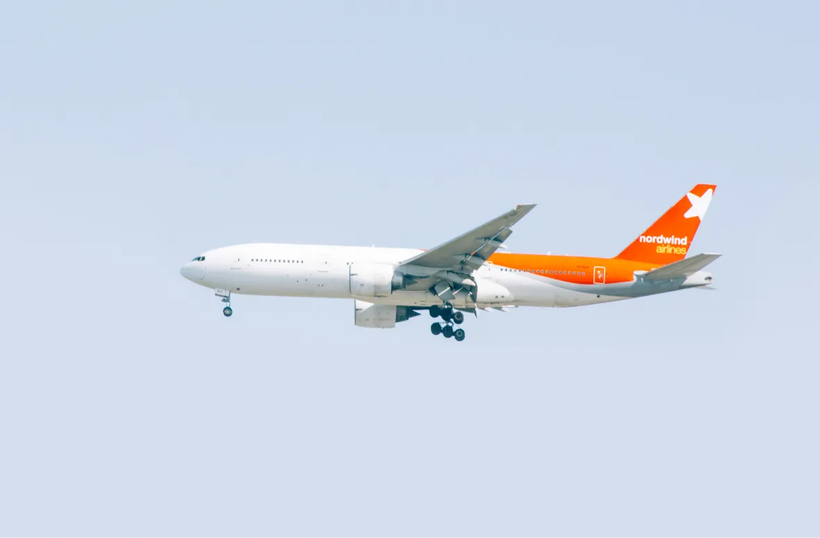 Airplane with an orange tail flying against a clear sky